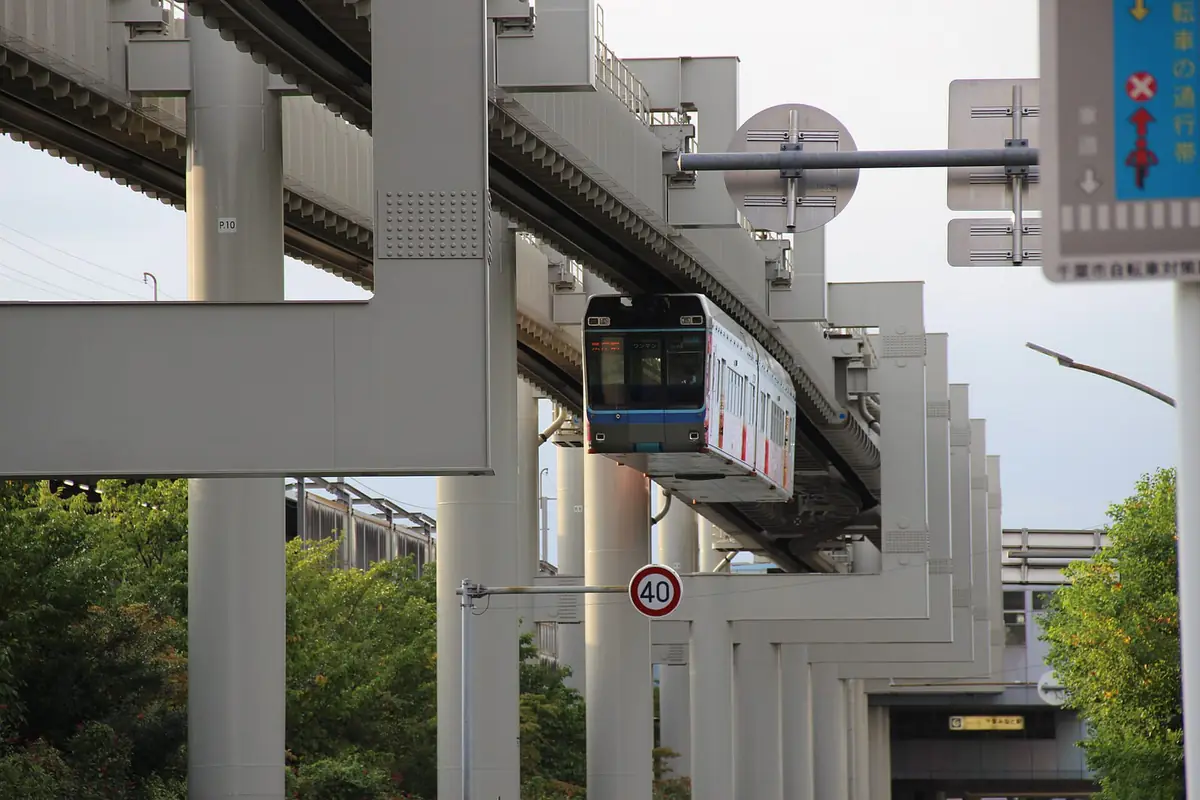頭上の軌道桁にぶら下がって走る千葉都市モノレールの車両。線路が地面になく、道路の上を進む懸垂式の構造が分かる