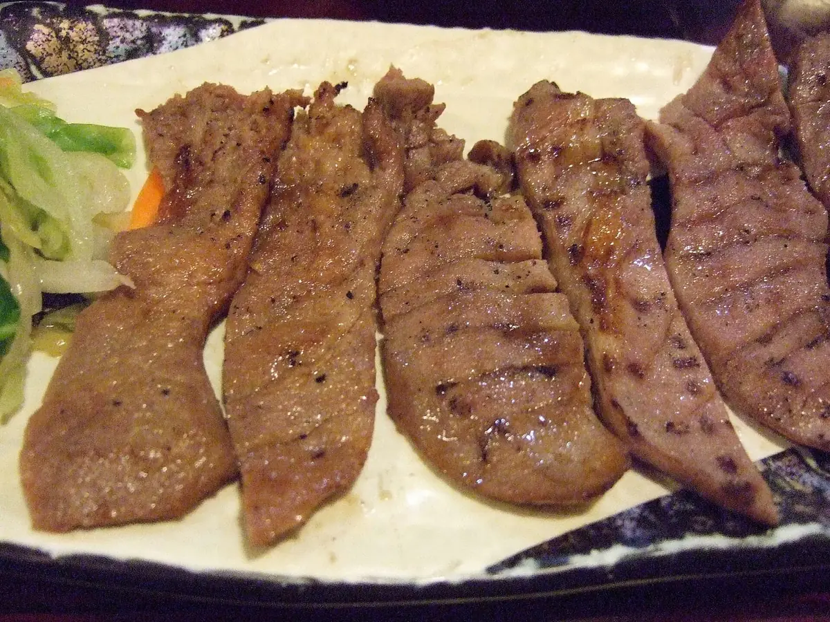 仙台名物の牛タン焼き。厚切りのタンが皿に並び、奥に浅漬けの野菜が添えられている