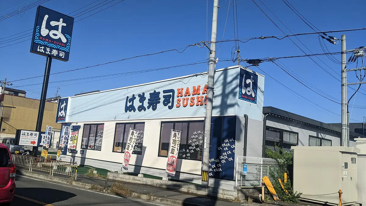 青空の下に建つ郊外型のはま寿司の店舗。屋根の看板と「は」のロゴポールが見える（記事の下関幡生店とは別の店）