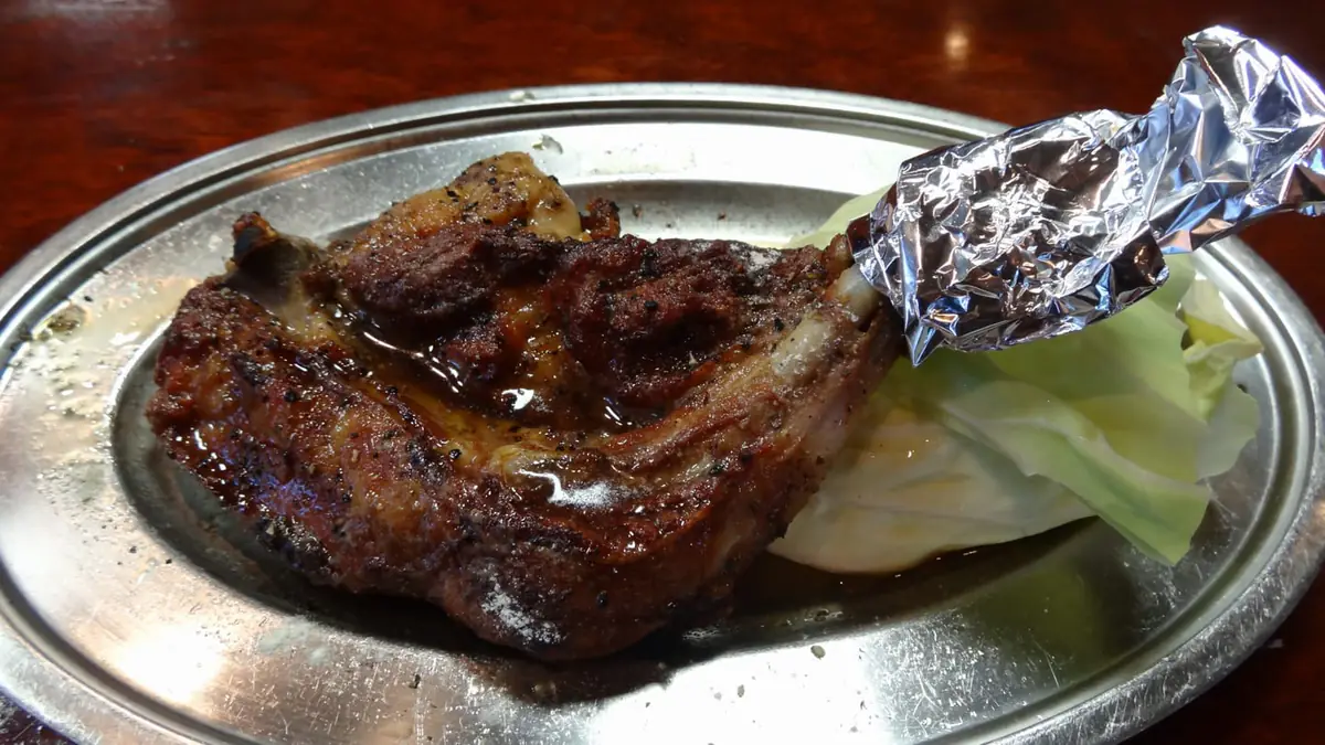 銀の皿にのった骨付き鳥。焼けた鶏もも肉から鶏油がにじみ、キャベツが添えられている