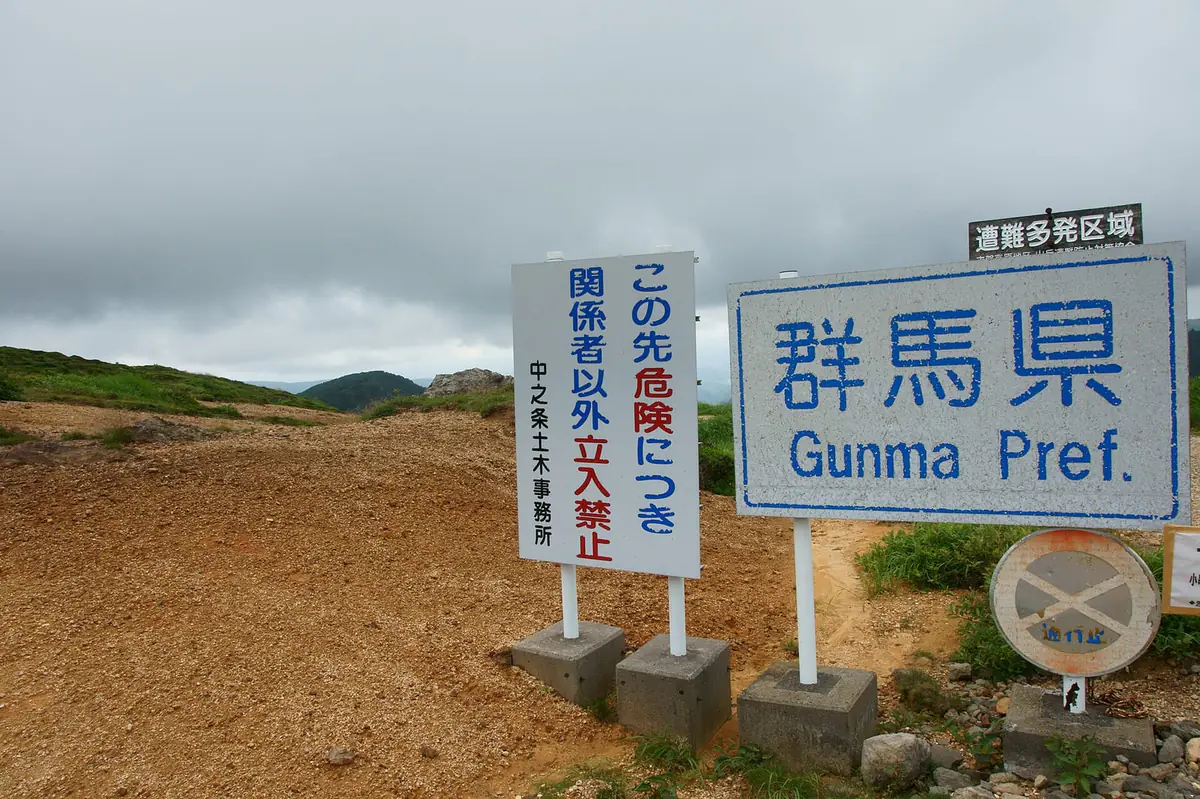 更新前の毛無峠の県境標識。青い文字の「群馬県 Gunma Pref.」看板と「関係者以外立入禁止」看板が荒れた地面に並ぶ