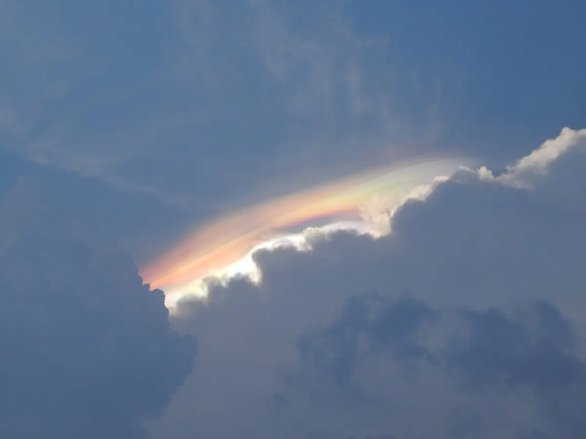 雲のふちが赤や緑に染まった彩雲。積乱雲の上に虹色の帯が横たわっている
