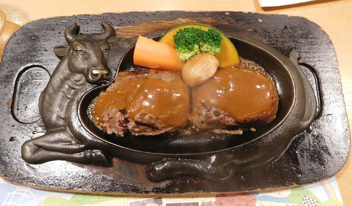 牛の形の鉄板の上で半分に割られた、さわやかのげんこつハンバーグ